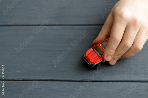 The hand of the child plays with a red typewriter on a wooden surface of a dark color.