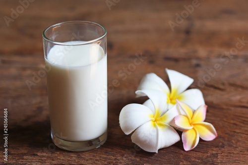 glass of milk and white flowers on wooden background
