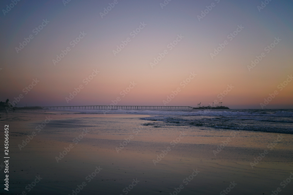 Soft pastel serene beach sunset at low tide with pier in distance