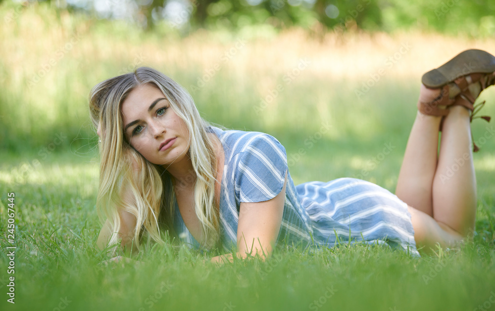 Stunning young blonde woman in summer dress laying on stomach in grass in shade Stunning young blonde woman in summer dress laying on stomach in grass in shade
