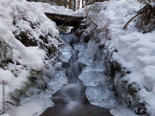 smooth motion of wild water in a river in winter with snow and ice on rocks and stones in the beautiful nature of a forest