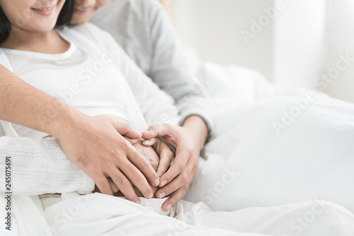 Cropped image of beautiful pregnant woman and her handsome husband hugging the tummy. Love couple hands make a heart on the pregnant belly.