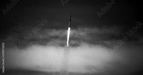 B&W footage (recreation) of cold war era ICBM missile rocket flying into space with exhaust flames, heat trail, and smoke in 4K.