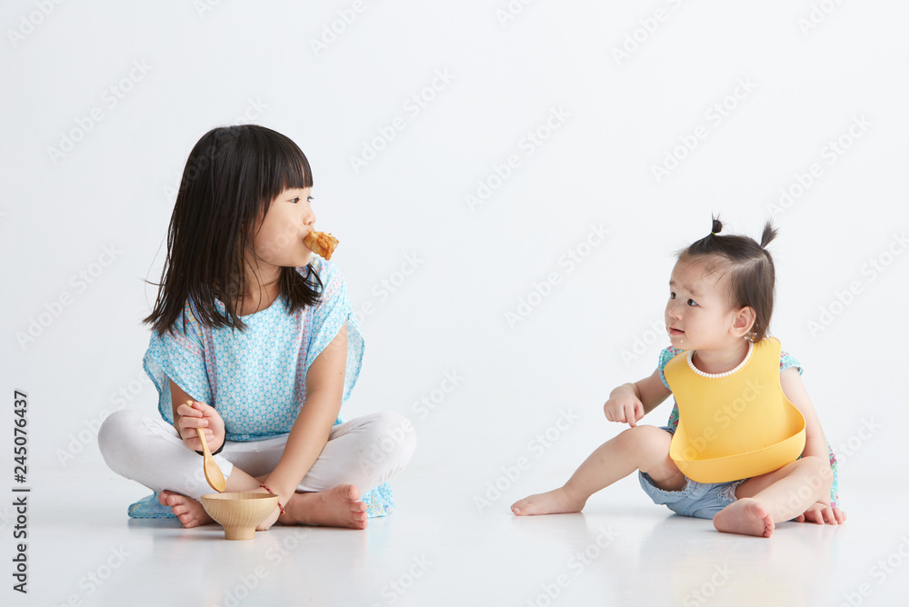 Asian little sisters eating together, in white background Asian little sisters eating together, in white background