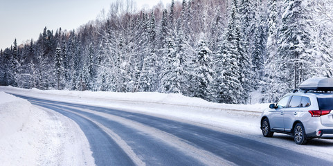 Suv car with rooftop cargo carrier trunk stay on roadside of winter road. Family trip to ski resort. Winter holidays adventure. car on winter road