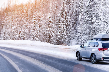 Suv car with rooftop cargo carrier trunk stay on roadside of winter road. Family trip to ski resort. Winter holidays adventure. car on winter road