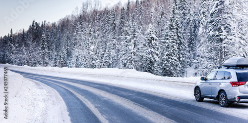 Suv car with rooftop cargo carrier trunk stay on roadside of winter road. Family trip to ski resort. Winter holidays adventure. car on winter road