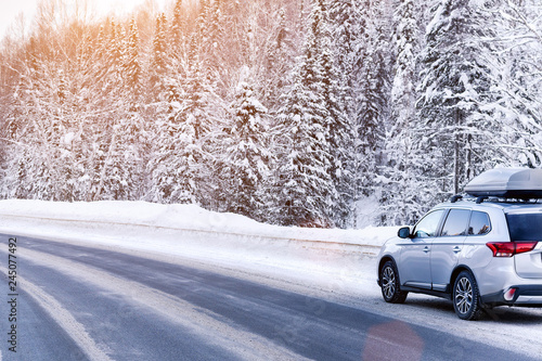 Suv car with rooftop cargo carrier trunk stay on roadside of winter road. Family trip to ski resort. Winter holidays adventure. car on winter road