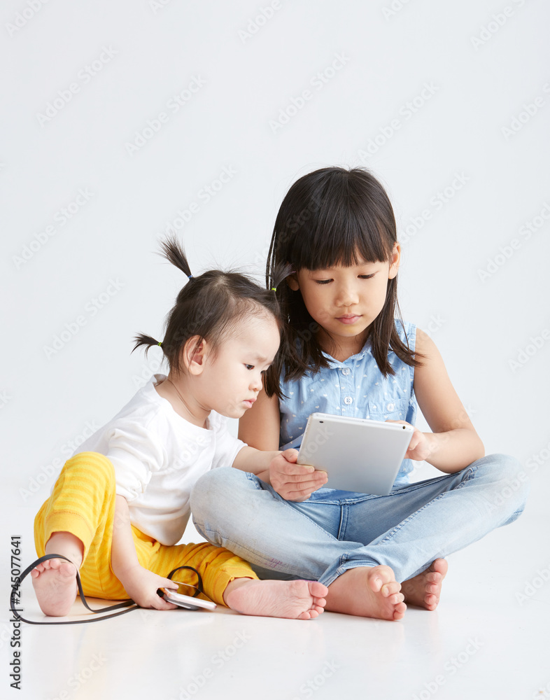 Asian little sisters are playing with digital gadgets, on white background Asian little sisters are playing with digital gadgets, on white background