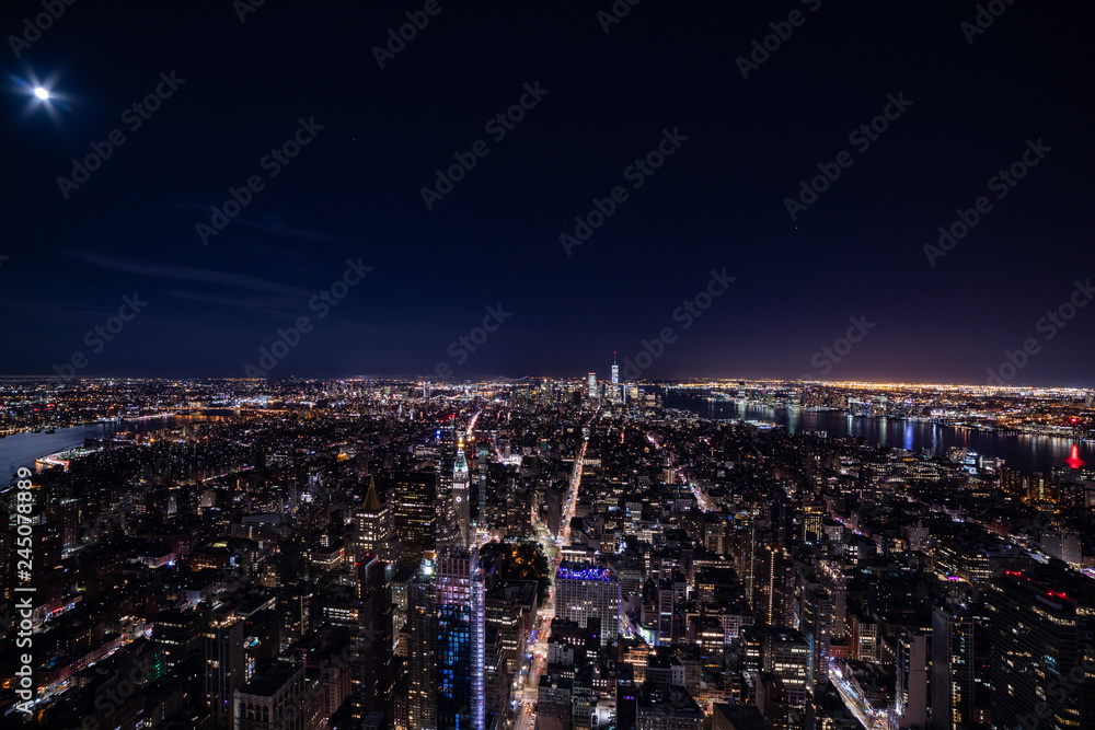 Magnificent skyline of a night New York.  Panoramic photo of midtown and Lower Manhattan with Easter and Hudson rivers. Moon shines in a dark sky