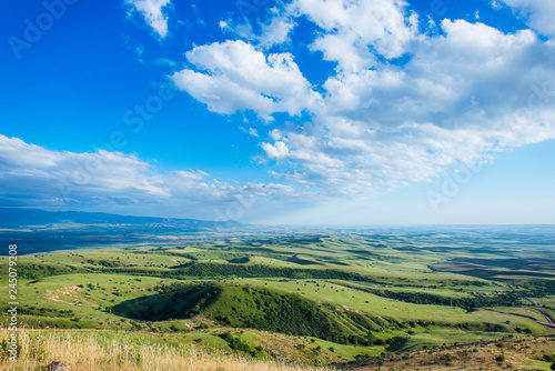 Blue sky with fluffy clouds. White cirrus clouds illuminated by the sun. Greenery small hills on the plateau. Earth meets the sky. Earth aerial view. Horizon away. Beautiful plain under the clouds. photo