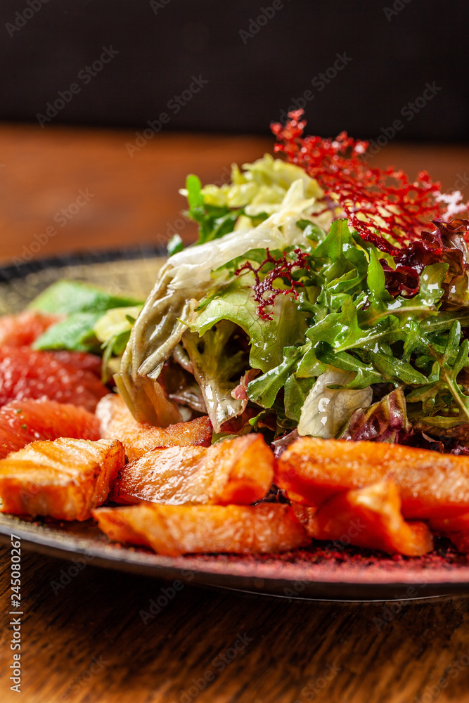 Modern Arabic cuisine in 2019. Asian salad of fried salmon, avacado, grapefruit and salad mix, with honey sauce. Serving dishes in a restaurant in a black plate with oriental spices. Modern Arabic cuisine in 2019. Asian salad of fried salmon, avacado, grapefruit and salad mix, with honey sauce. Serving dishes in a restaurant in a black plate with oriental spices.