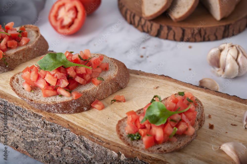 Bruschetta sandwiches with tomato, basil leaf and garlic on wooden board as background