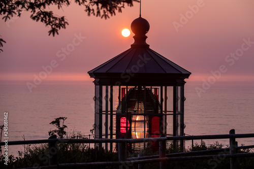 Sun setting down behind Cape Meares lighthouse photo