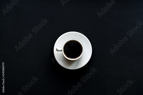 top view of white cup of coffee on black background. Minimal flat lay.