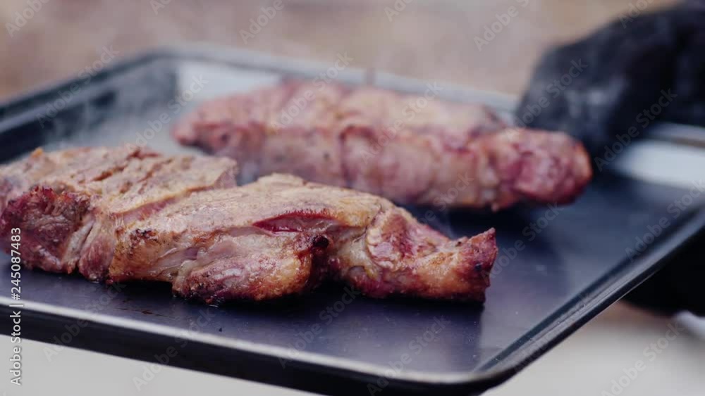 Gloved hand holds recently cooked cuts of meat on a tray outside Gloved hand holds recently cooked cuts of meat on a tray outside