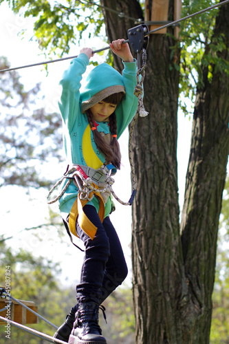 A girl in a hood on a platform for mountaineering on a hanging road. Rope Park