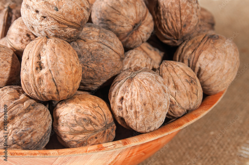 Many walnuts lie in a bowl. Bowl on burlap. Close-up. Many walnuts lie in a bowl. Bowl on burlap. Close-up.