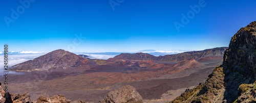 Scenic panorama of a Haleakala volcano. White clouds enters into the valley with dark brown cinder cones. View from above the clouds line © Dmitry