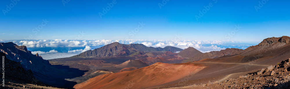 Scenic panorama of a Haleakala volcano from Keonehe'ehe'e trail overlooking cinder cones inside a caldera. Clear blue sky white puffy clouds below the horizon and rich red-brown colors of a mountain