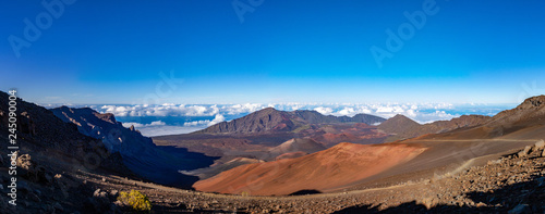 Scenic panorama of a Haleakala volcano from Keonehe'ehe'e trail overlooking cinder cones inside a caldera. Clear blue sky white puffy clouds below the horizon and rich red-brown colors of a mountain