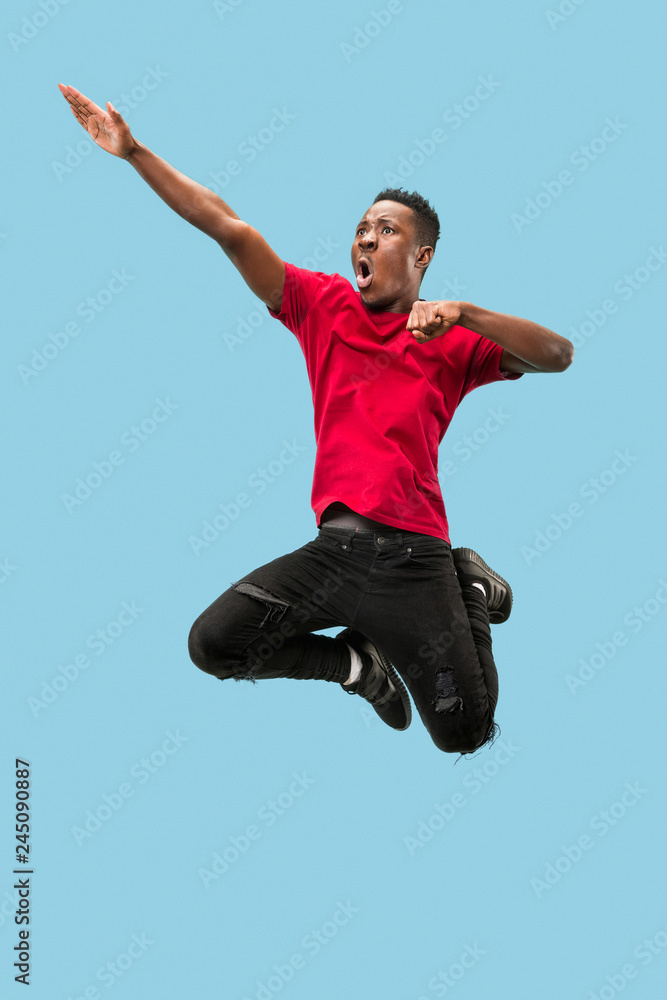 Forward motion. The happy surprised young african man jumping against blue studio background. Runnin man in motion or movement. Human emotions and facial expressions Forward motion. The happy surprised young african man jumping against blue studio background. Runnin man in motion or movement. Human emotions and facial expressions
