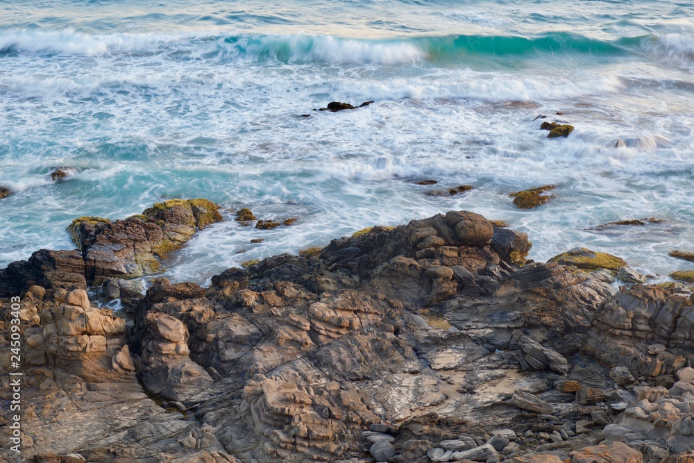 High angle photo of blurred waves crashing onto sunlit rocks High angle photo of blurred waves crashing onto sunlit rocks