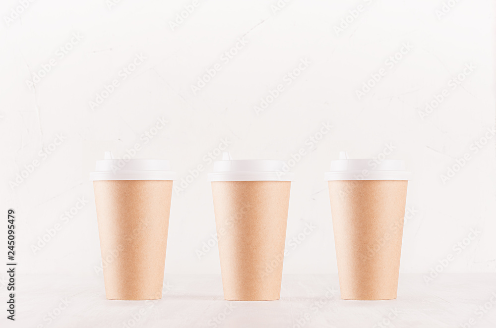 Coffee packing mockup - set of three kraft brown paper cups with white cap on white wood board, coffee shop interior. Modern elegant concept for branding identity, advertising, design. Coffee packing mockup - set of three kraft brown paper cups with white cap on white wood board, coffee shop interior. Modern elegant concept for branding identity, advertising, design.