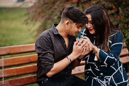 Love story of indian couple posed outdoor, sitting on bench together.