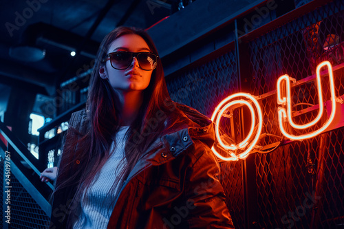 Young stylish girl wearing a hoodie coat and sunglasses standing on stairs at underground nightclub with industrial interior