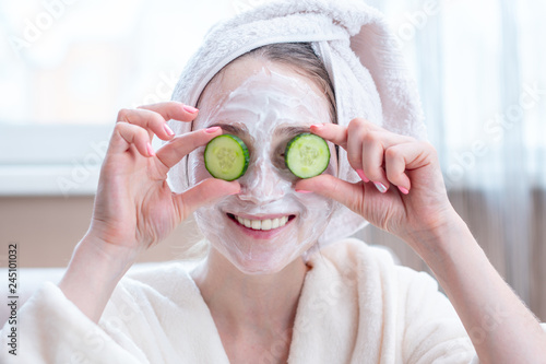 Beautiful young woman with natural cosmetic mask and cucumber slices on her face. Skin care and Spa treatments at home