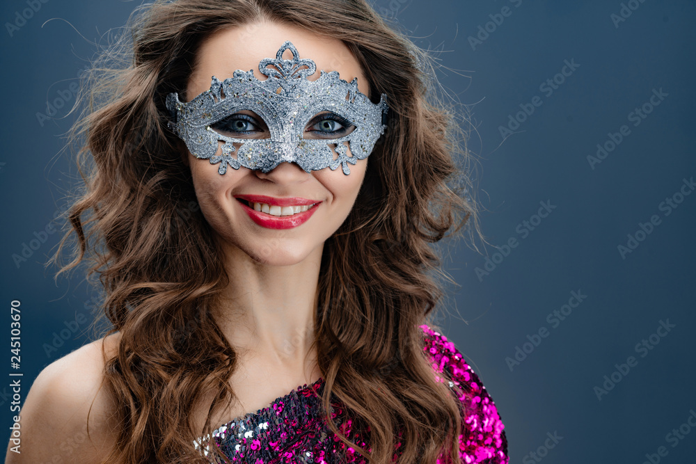 Girl with beautiful hair styling in a Venetian carnival mask on a blue background close-up. - Image