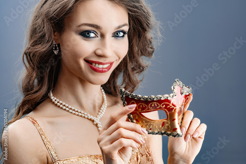  Young woman in a pearl necklace smiles holds a carnival mask in her hand close-up