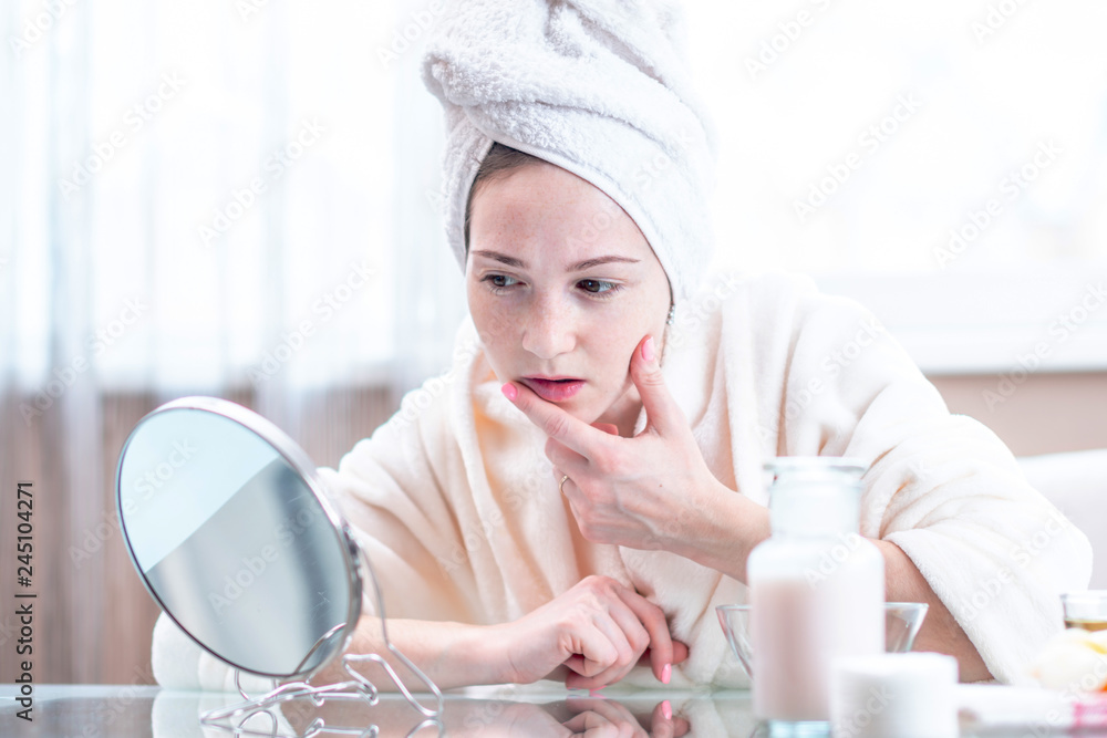 Beautiful happy woman with a towel on her head looking at her skin in a mirror. Concept of hygiene and care for the skin Beautiful happy woman with a towel on her head looking at her skin in a mirror. Concept of hygiene and care for the skin