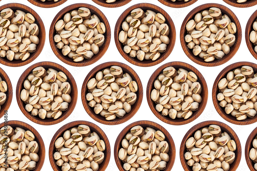 Unpeeled pistachios in a wooden cedar plate on a white isolated background. Row of bowls with pistachio nuts, top view. Unpeeled pistachios pattern Unpeeled pistachios in a wooden cedar plate on a white isolated background. Row of bowls with pistachio nuts, top view. Unpeeled pistachios pattern