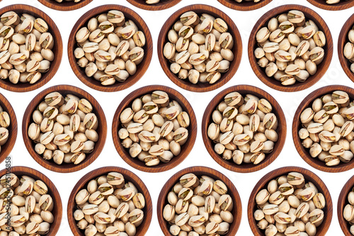 Unpeeled pistachios in a wooden cedar plate on a white isolated background. Row of bowls with pistachio nuts, top view. Unpeeled pistachios pattern
