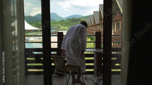 Stable 4K shot of a Caucasian man in a bathrobe stepping out on a patio to overlook a beautiful spa resort in Besenova, Slovakia. photo