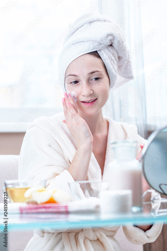 Beautiful happy young woman applying cream on face moisturizing the skin. Hygiene and care for the skin at home Beautiful happy young woman applying cream on face moisturizing the skin. Hygiene and care for the skin at home