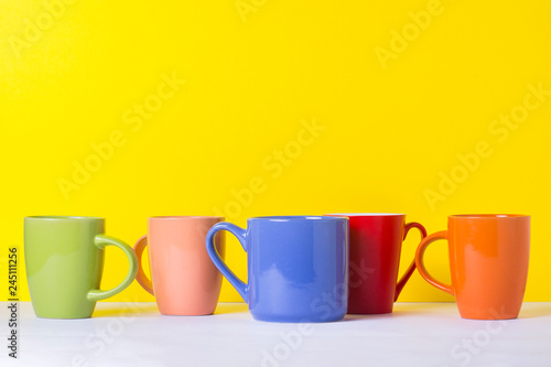 A lot of multicolored cups of coffee or tea on a yellow background. The concept of a friendly company, a large family, meeting friends for a cup of tea or coffee