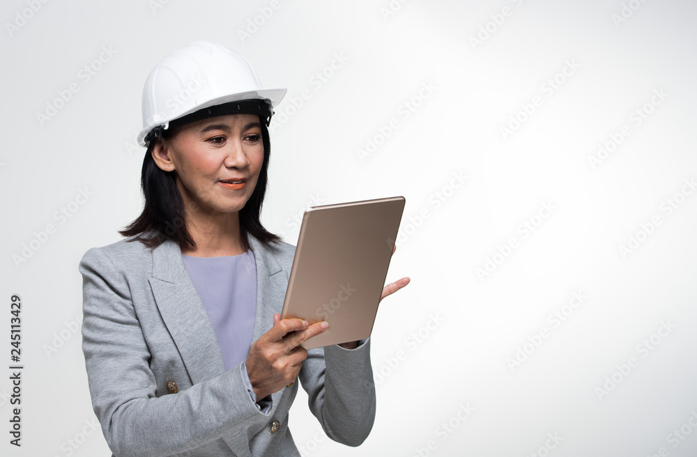 Beautiful Asian Smart Architect Engineer 50s 60s years old woman in white hard hat helmet hold tablet iot, portrait studio lighting gray background copy space, concept aging society woman can do Beautiful Asian Smart Architect Engineer 50s 60s years old woman in white hard hat helmet hold tablet iot, portrait studio lighting gray background copy space, concept aging society woman can do