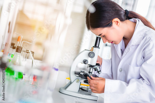 Scientist sing microscope in laboratory with lab glassware containing chemical liquid, science or medical research and development concept 