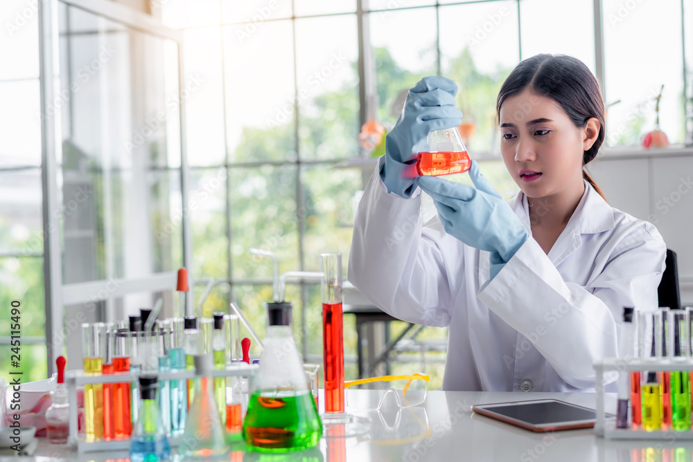 Attractive scientist looking chemical sample in flask at laboratory with lab glassware background. Science or chemistry research and development concept. Attractive scientist looking chemical sample in flask at laboratory with lab glassware background. Science or chemistry research and development concept.
