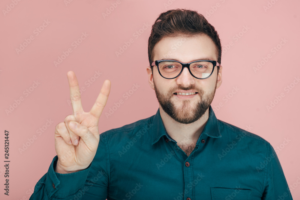 Naklejka premium a man with a beard in glasses and a shirt shows two on his fingers