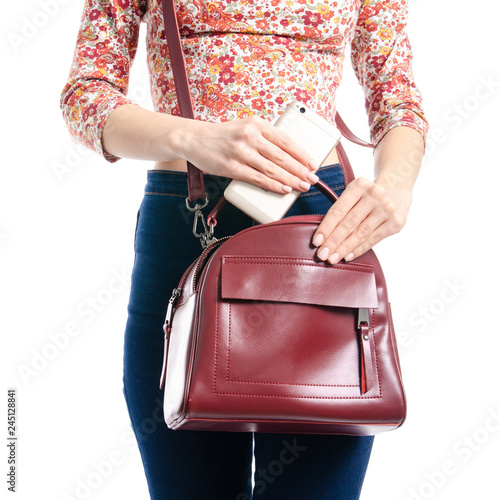 Woman in blue jeans and shirt put smartphone in red bag macro on white background isolation