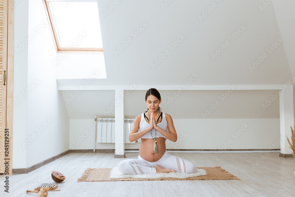 Pregnant woman meditates indoor in home interior in yoga pose. Woman enjoying in meditation. Pregnant woman meditates indoor in home interior in yoga pose. Woman enjoying in meditation.