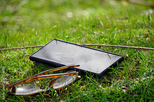 Smartphone and glasses on green lawn on a sunny day