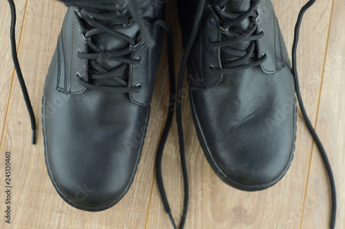 a pair of Russian military boots with signs of wear and dust on the wooden floor, close, top view