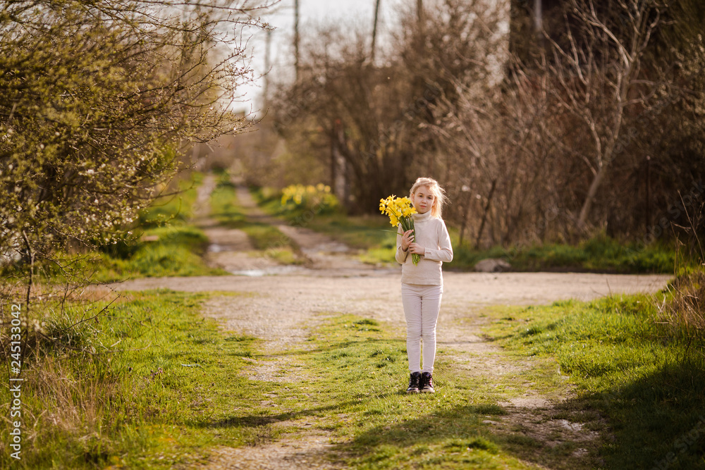 Fototapeta premium cute blonde happy little girl with yellow daffodils in the spring country