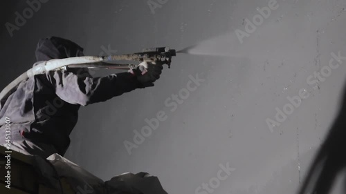 Close up: industrial worker sprays polyurea to the concrete surface with a pressure gun. Industrial process of waterproofing with polyurea. A man in a protective form and respirator. photo