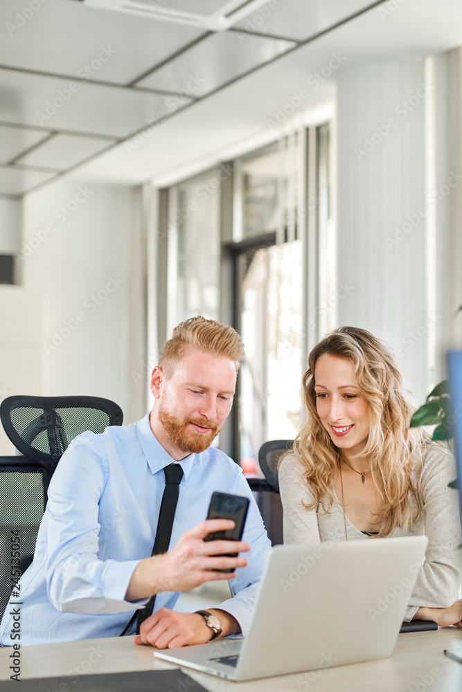 Two colleagues working in office, he is showing something to her on his smartphone Two colleagues working in office, he is showing something to her on his smartphone